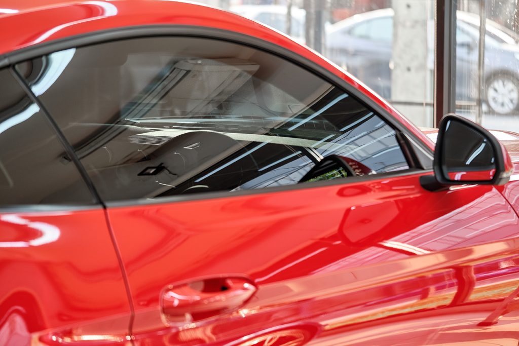 Close up of car window tint. Ceramic film provide heat rejection & UV protection with color stable shade. Automobile film installed to glass surface of red car. Professional tinting service background