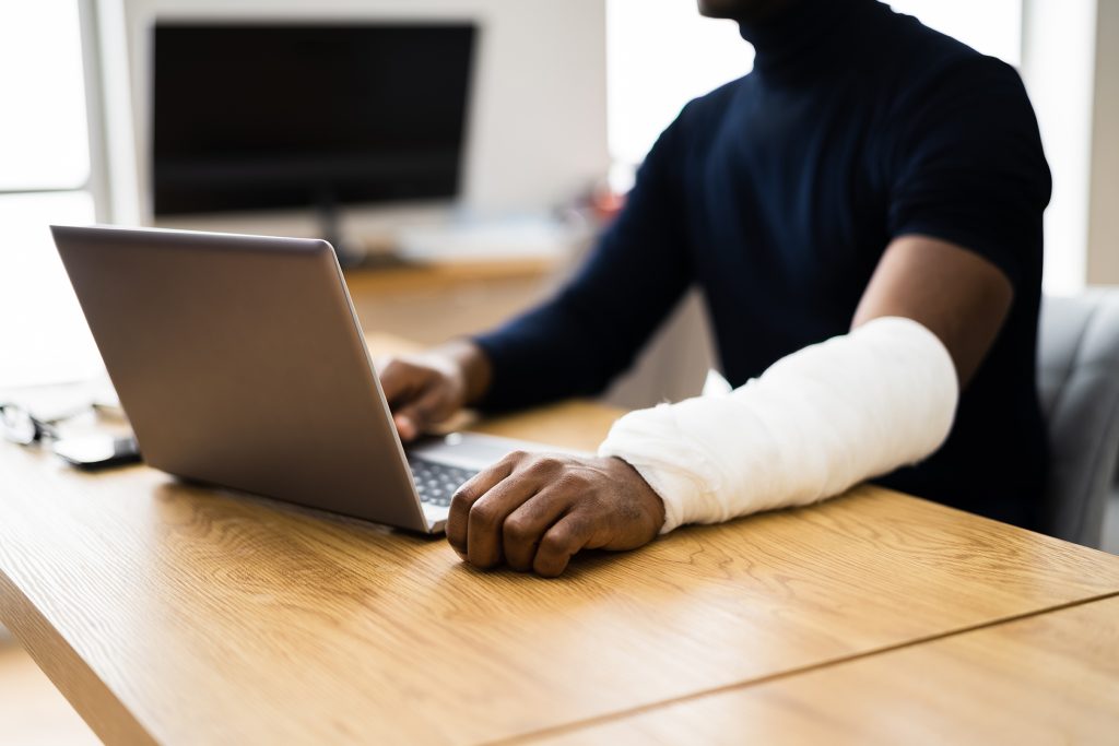 Injured Worker Compensation. Broken Arm African Man On Computer