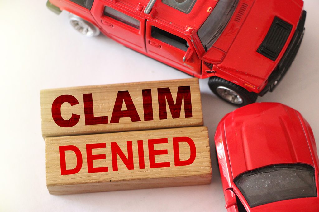 Claim denied words on wooden blocks and two red cars in road accident on white. Insurance concept, negative answer from insurance company.