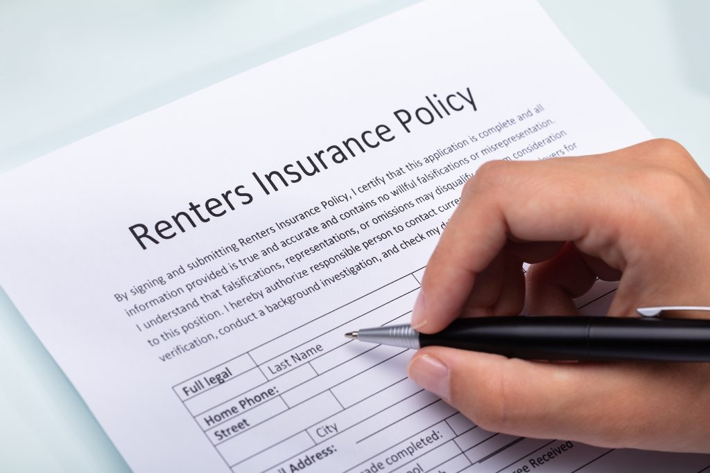 Close-up Of A Person's Hand Filling Renters Insurance Policy Form