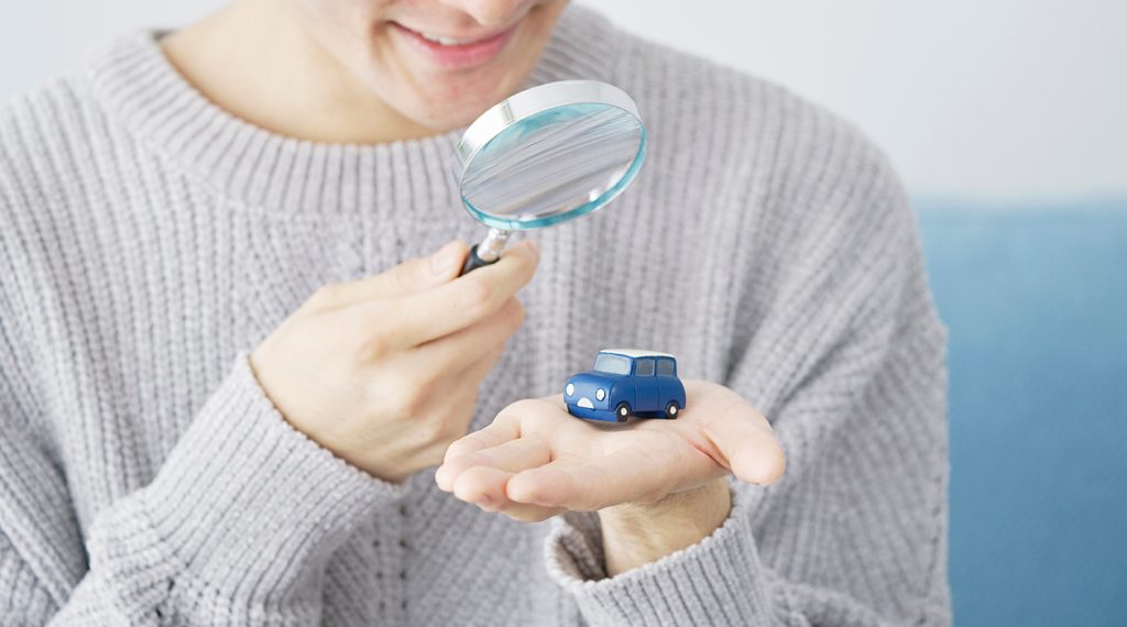 Asian man looking at a miniature car with a magnifying glass