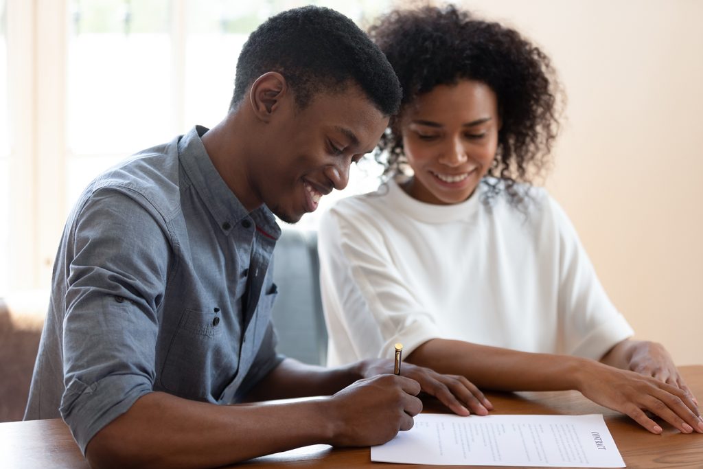 Satisfied African ethnicity couple affirming prenuptial contract, smiling husband putting signature on lease agreement, young family taking loan in bank filling form, health insurance buyers concept