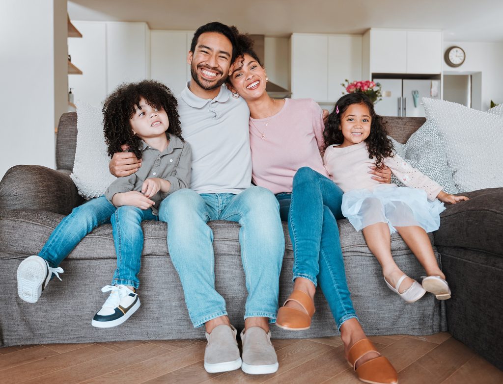 Portrait of mother, father and kids on sofa together, happy family bonding in living room with love and support. Smile, happiness and parents relax with kids on couch, spending quality time in home.